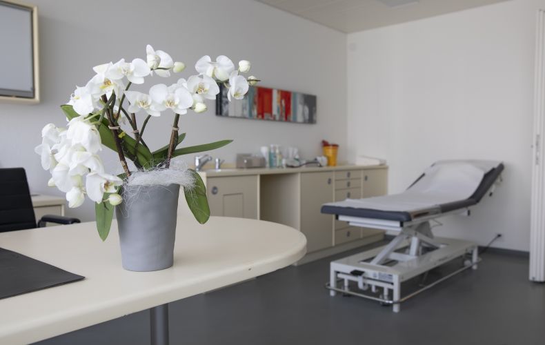 Behandlungsraum mit Orchideen auf dem Tisch links und Behandlungsliege rechts